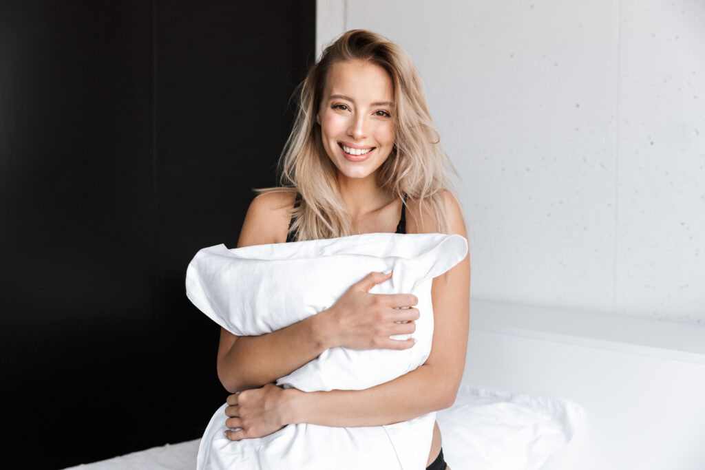 Photo d'une magnifique jeune femme en sous-vêtements de lingerie le matin au lit à la maison tenant un oreiller.