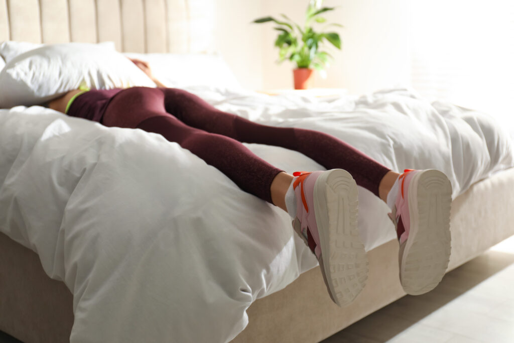 Une jeune femme paresseuse dort sur son lit au lieu de s'entraîner le matin, se concentre sur ses jambes