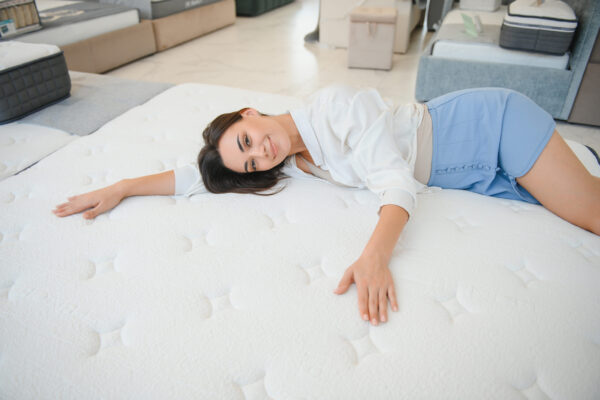 une femme brune heureuse est assise sur un matelas pour le tester dans le magasin.